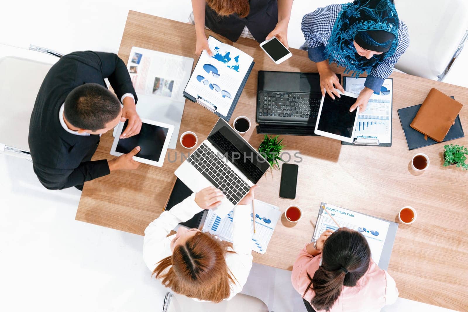 Top view of businessman executive in group meeting with other businessmen and businesswomen in modern office with laptop computer, coffee and document on table. People corporate business team uds