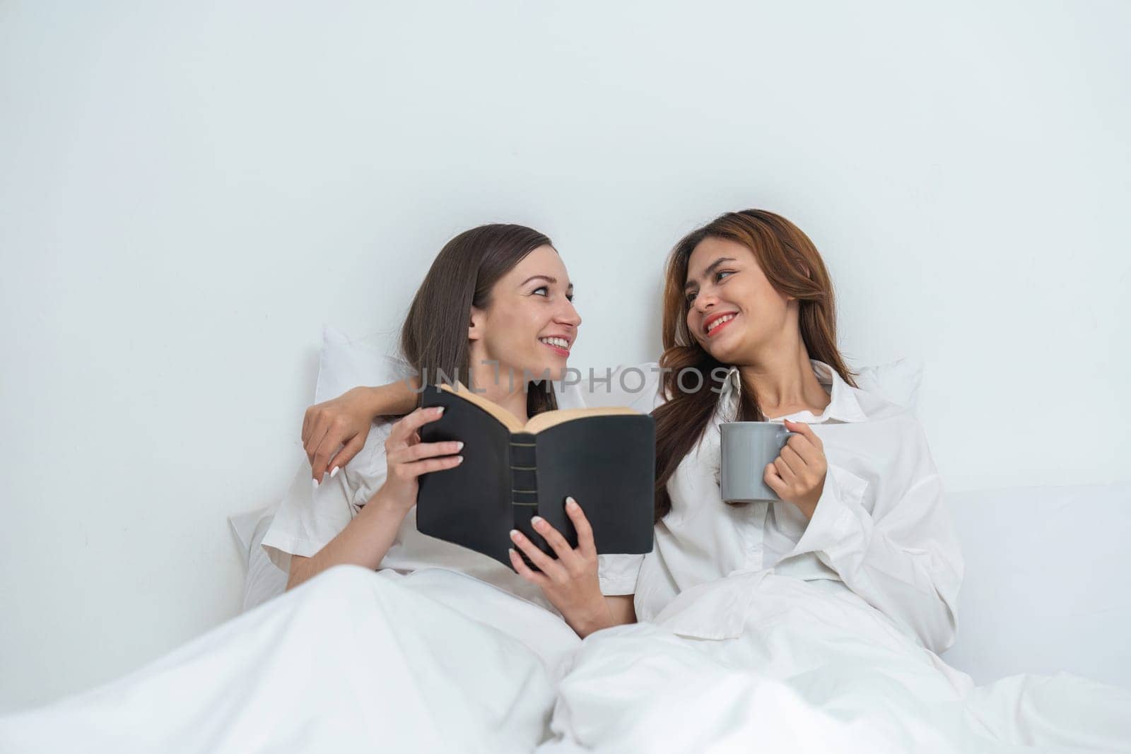 Young Asian lesbian couple sitting on bed during happy resting time Talk and relax in the bedroom. by wichayada