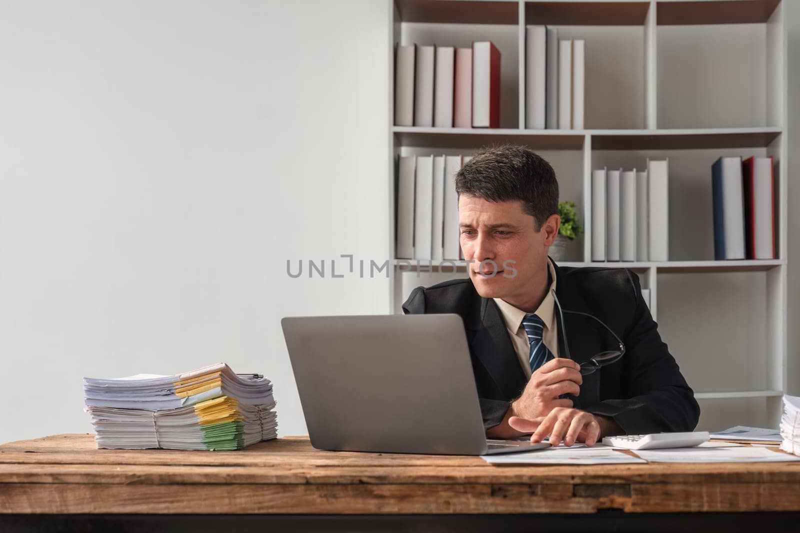 Unhappy young businessman feeling bored and stressed at work looking at laptop with hopeless expression while sitting in office.