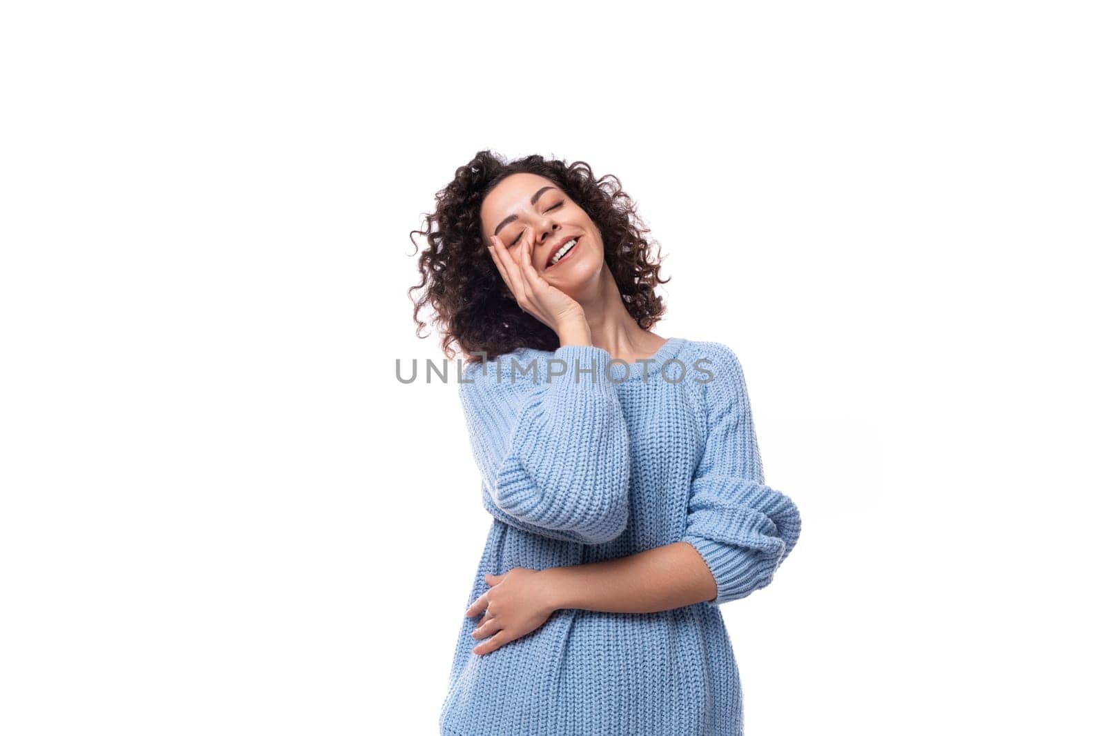 a young caucasian woman with curly dark hair is dressed in a casual warm blue sweater by TRMK