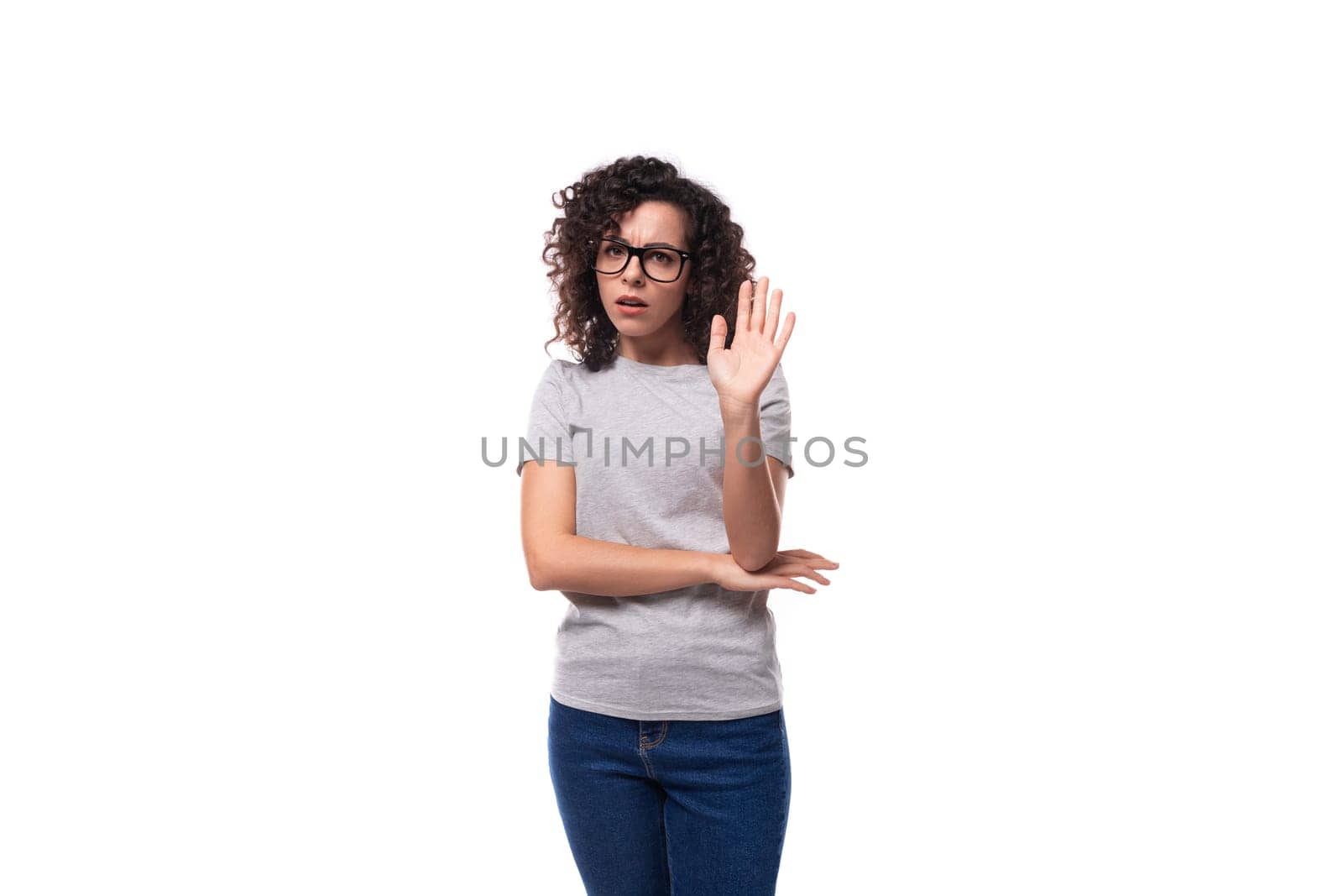 young cute pretty brunette curly caucasian lady in glasses dressed in casual jeans and a t-shirt raises her hand to say news by TRMK