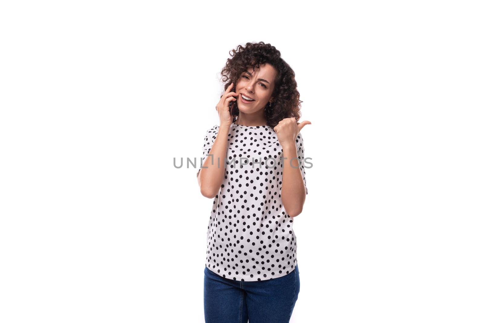 a slender young stylish woman with a curly haircut dressed in a blouse with polka dots speaks on the phone.