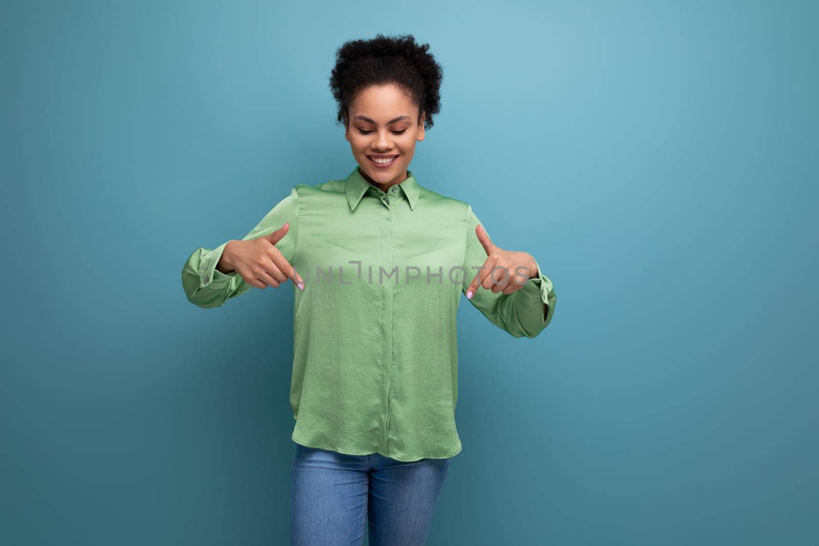 young cheerful latin business lady in green blouse showing hands down on studio background with copy space.
