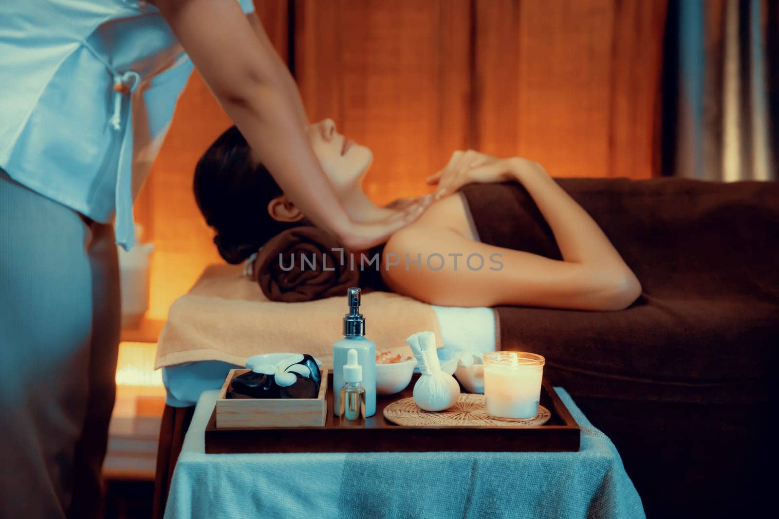 Aromatherapy massage ambiance or spa salon composition setup with focus decor candles and spa accessories on blurred woman enjoying blissful aroma spa massage in resort or hotel background. Quiescent