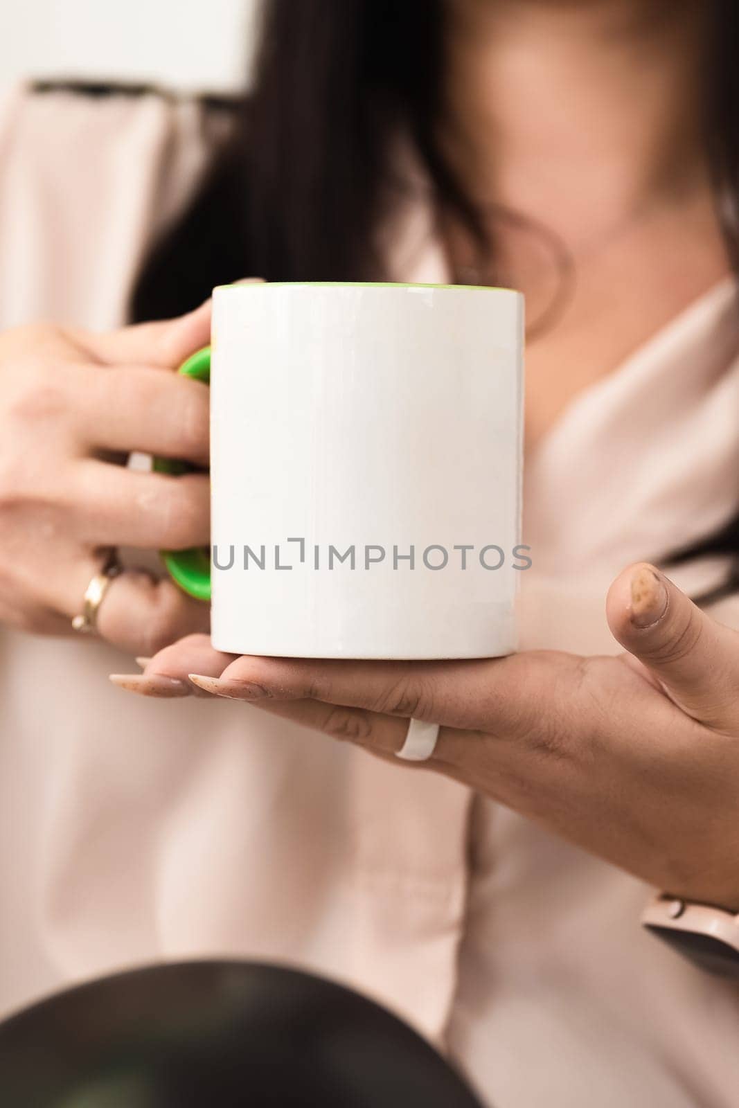 A brunette girl holds in her hands a ceramic white mug without a pattern for applying her logo or advertising