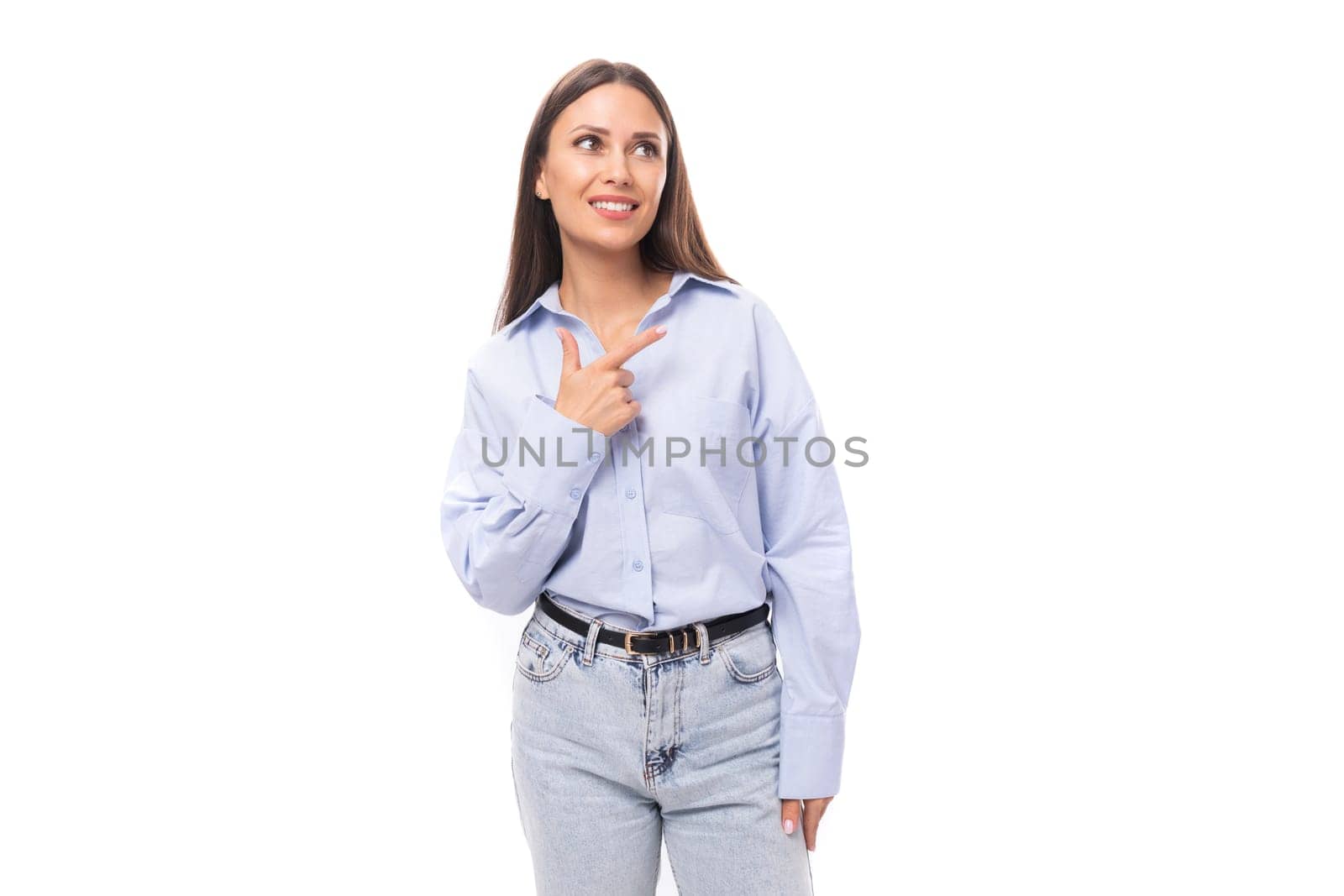 attractive young brunette caucasian woman dressed in a sky blue shirt looks attentively to the side on a white background with copy space.