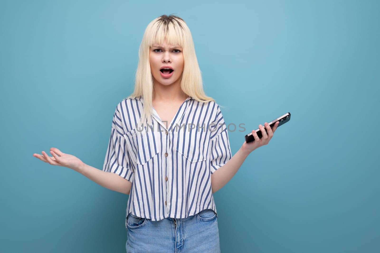 pretty european 20s woman in a striped shirt with a mobile phone in her hands on a studio background.