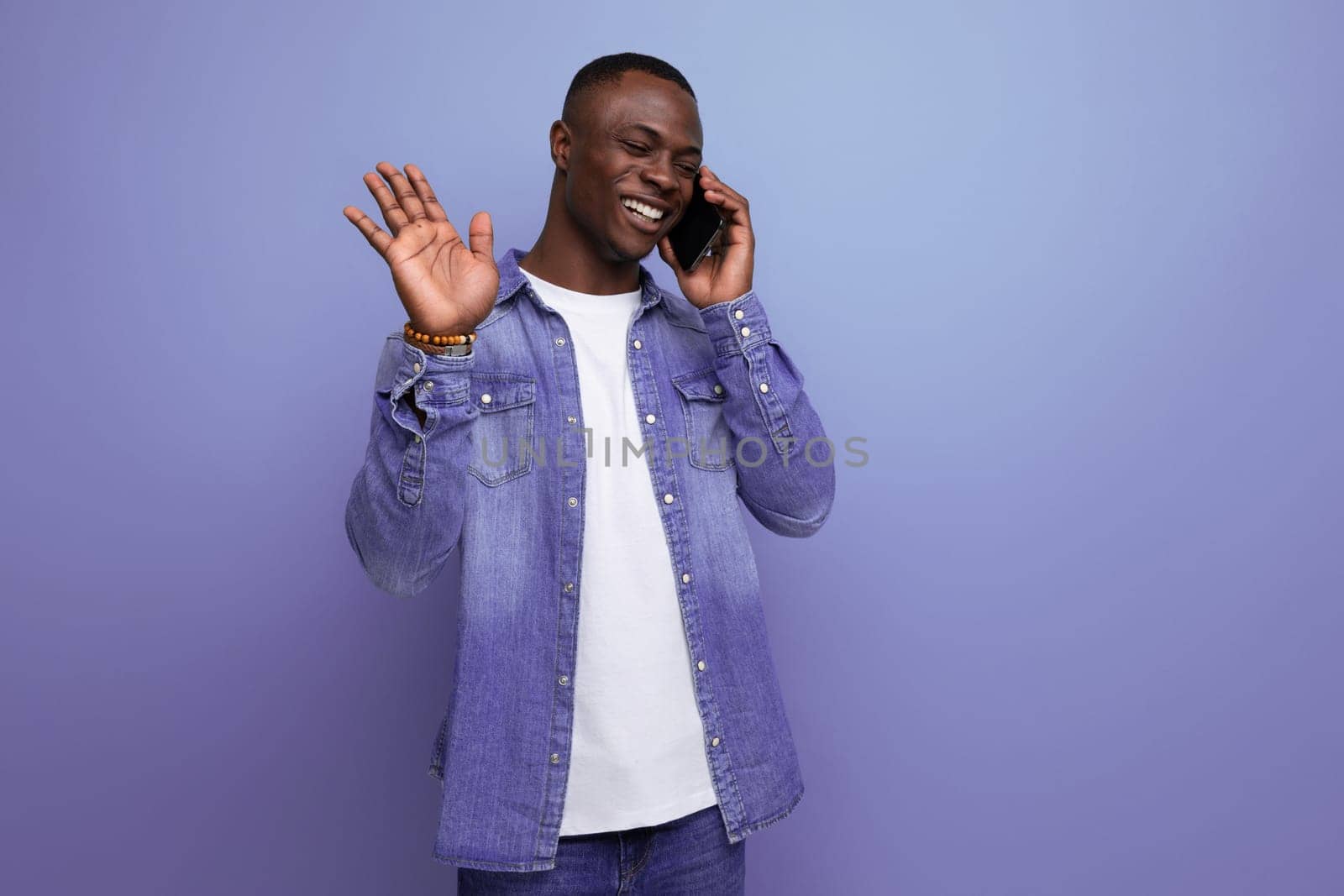 portrait of a well-groomed emotional young attractive african man dressed casually in denim clothes chatting on the phone by TRMK