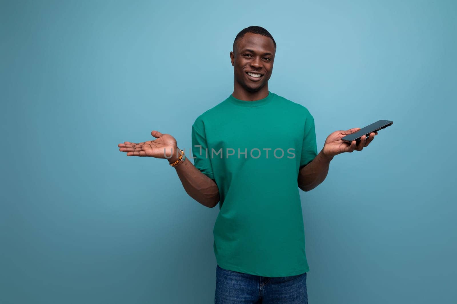 30 year old dark-skinned American man wearing a green T-shirt holding a smartphone in his hand.