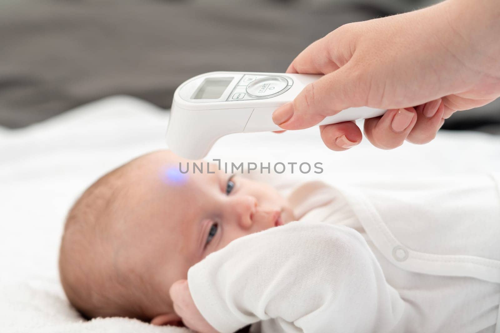 Mother attentively measuring her infant baby's temperature using a digital thermometer aimed at the