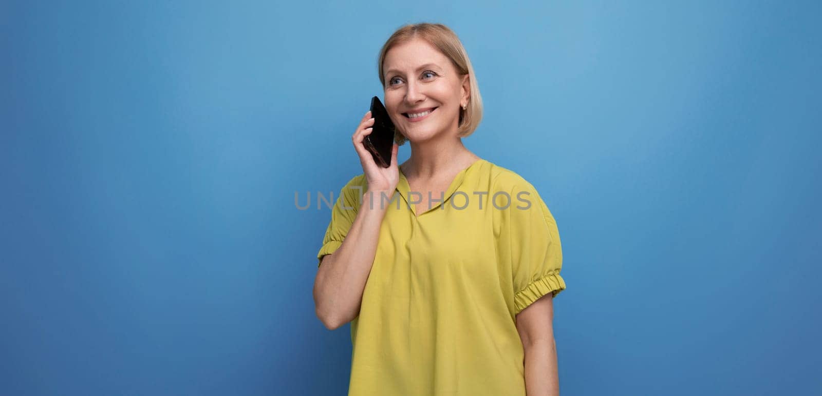 blond middle aged woman chatting on the phone in studio background.