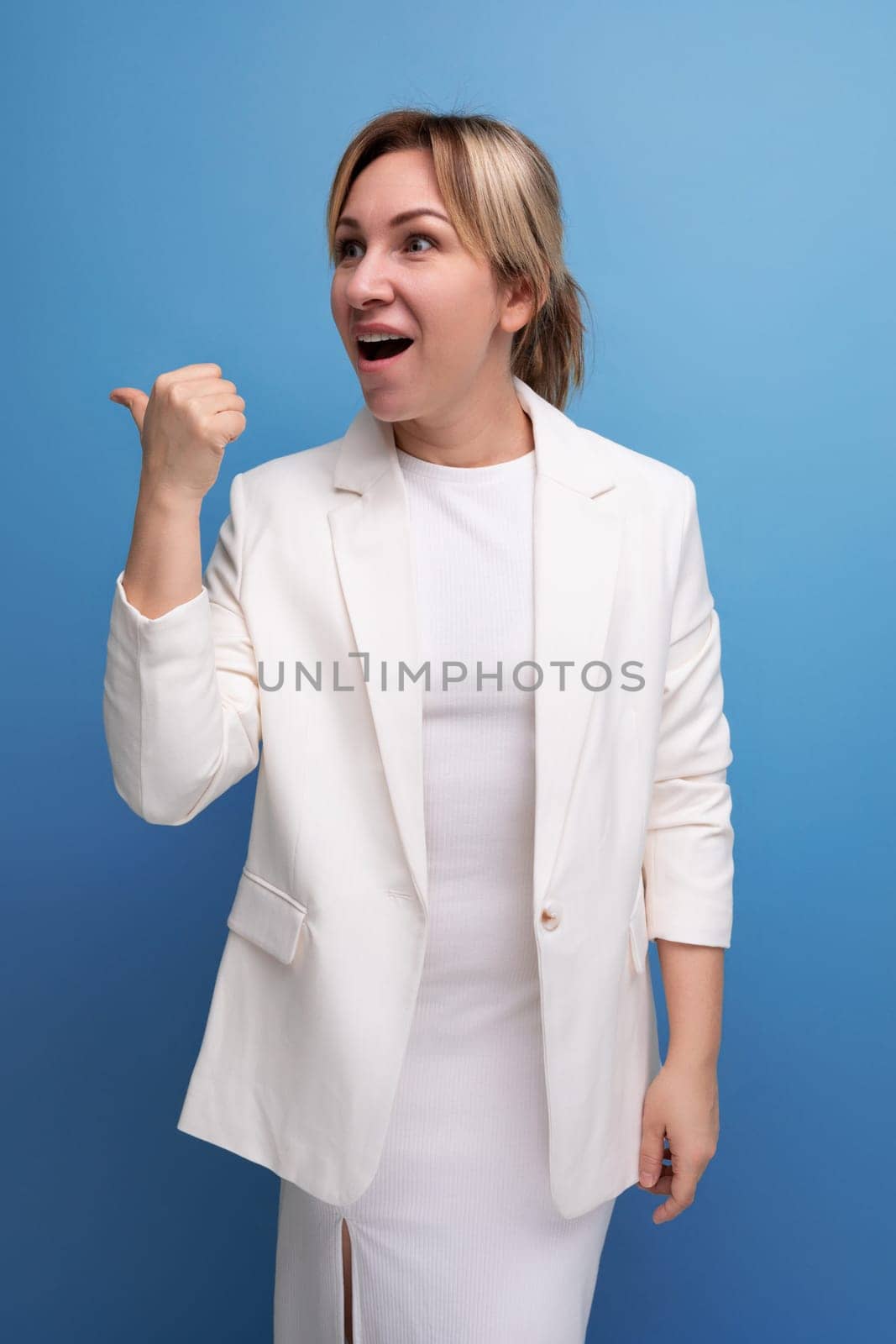 well-groomed young Caucasian blond lady in a white jacket and dress shows her fingers to the sides.