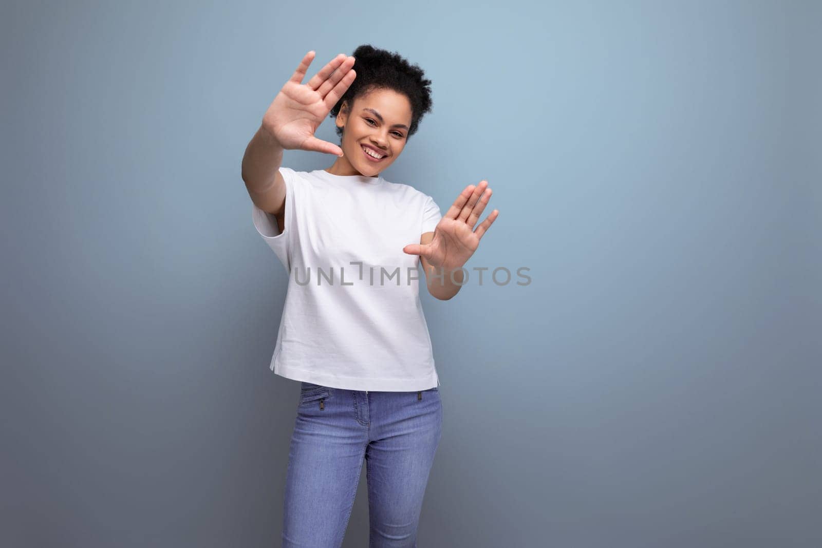 surprised young brunette woman with afro hair in a white t-shirt uses her hands for gesticulation and communication by TRMK