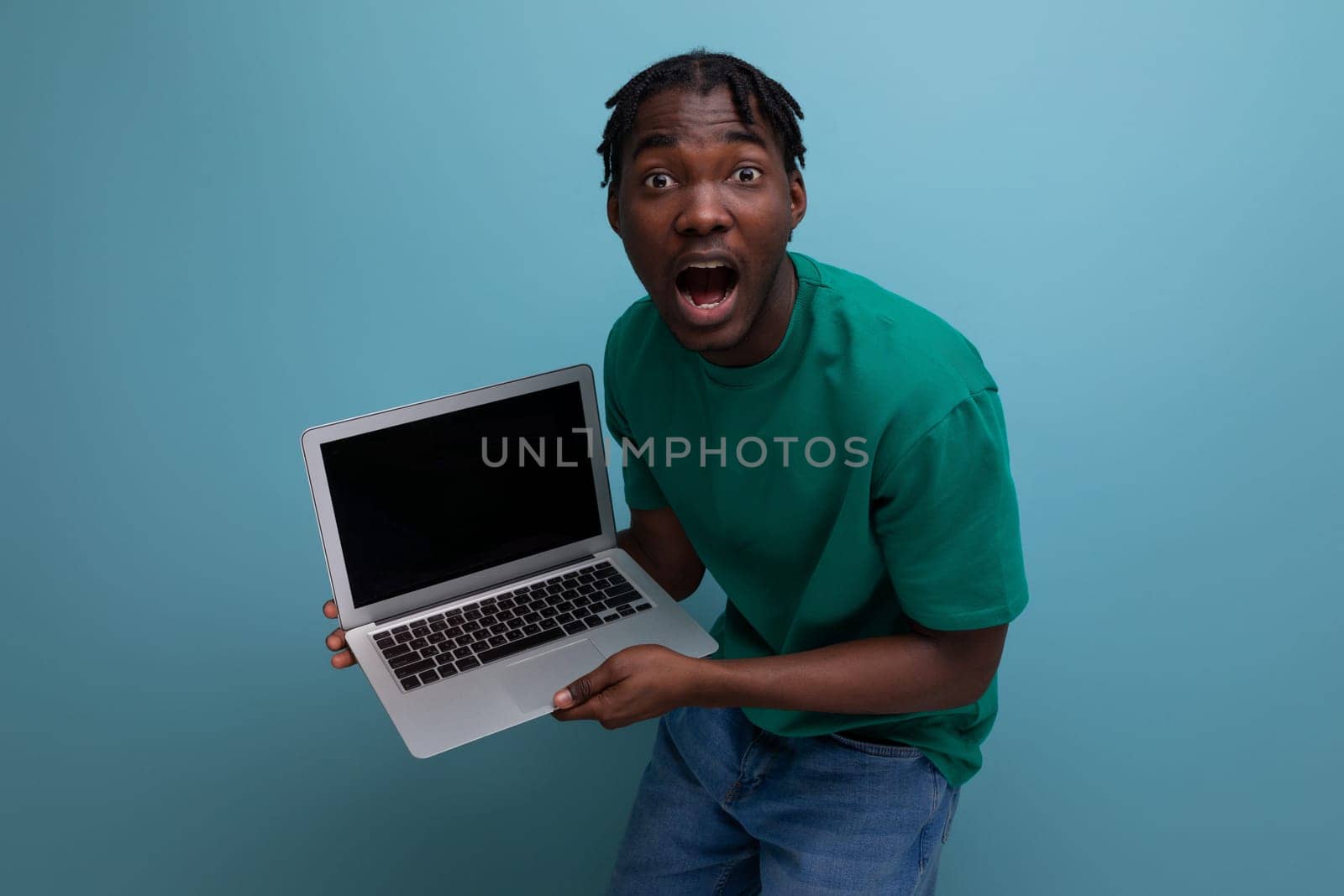surprised joyful african young brunette male consultant in casual t-shirt with open laptop by TRMK