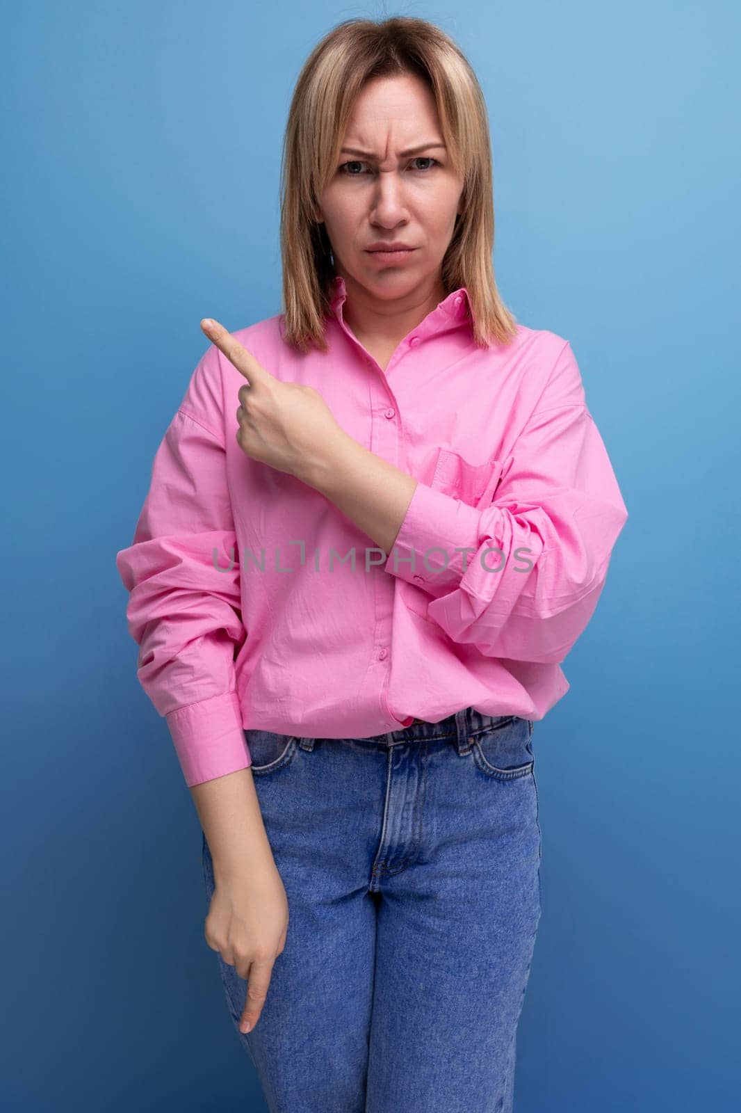 young successful blond careerist leader woman in a pink blouse shows her hands towards the empty space for advertising.