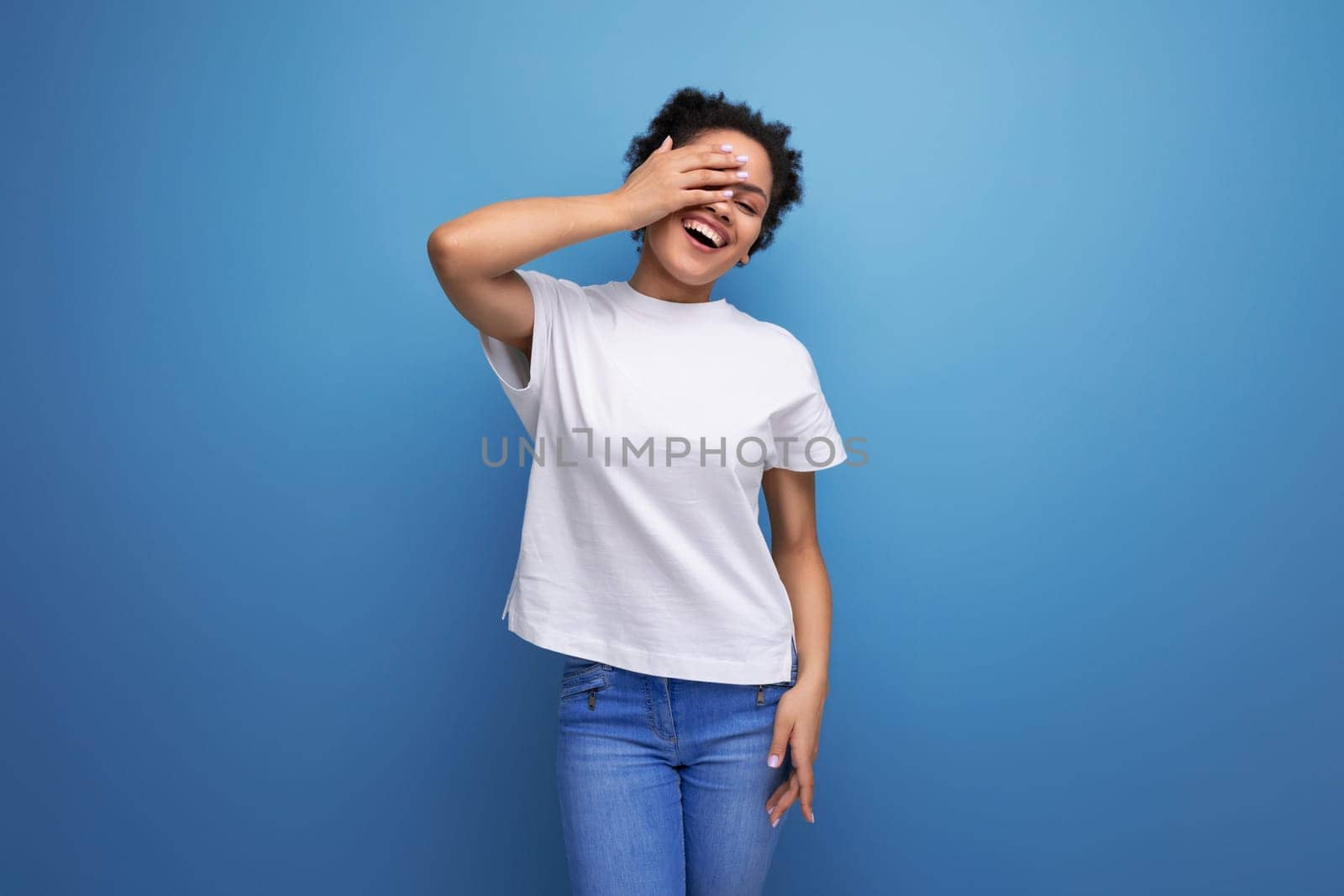 young brunette woman with afro hair in white t-shirt on studio background with copy space.