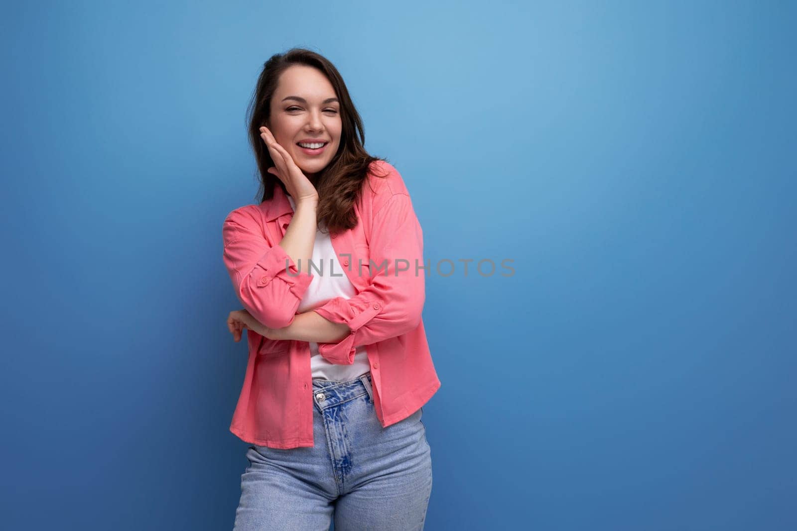 stylish brunette woman in trendy shirt rejoices on studio background.