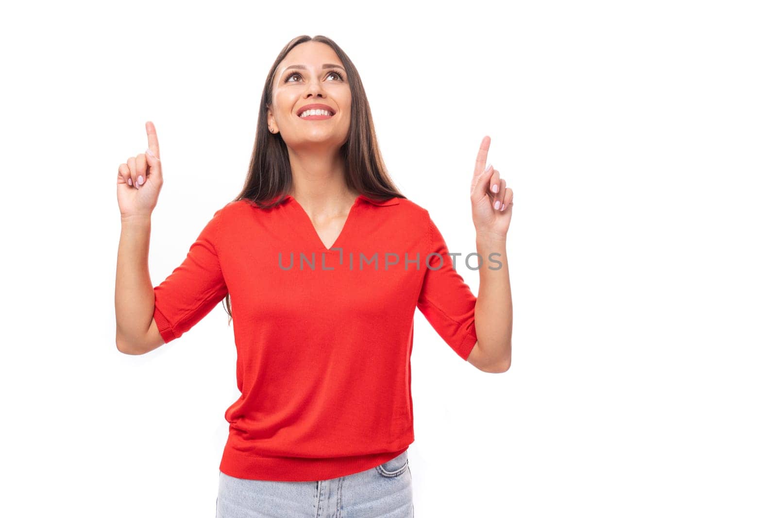 young caucasian female model with black straight hair dressed in a red t-shirt points with her hand at the empty space.