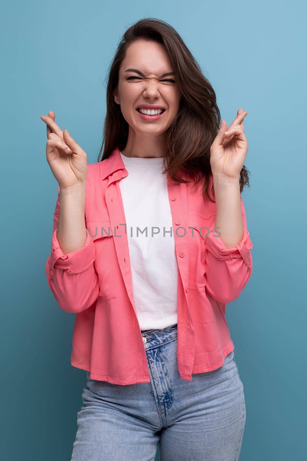 positive brunette lady with dark hair below her shoulders in a shirt and jeans crossed her fingers in anticipation of a surprise.