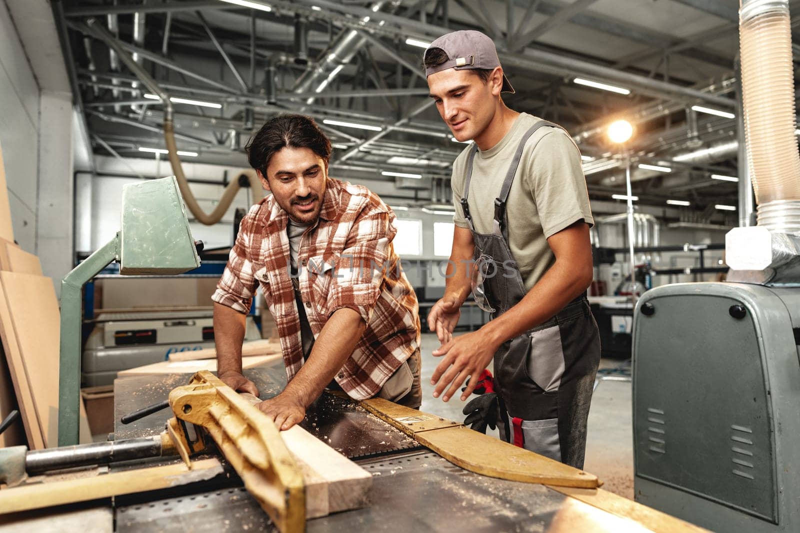 Two young carpenters working with wood standing at table in workshop close up