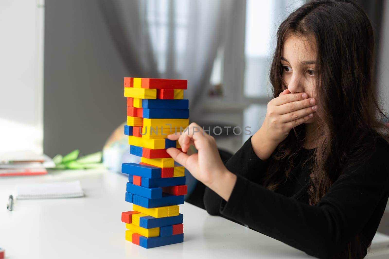 a little girl play a board game jenga at the table. Construction of a tower from wooden cubes