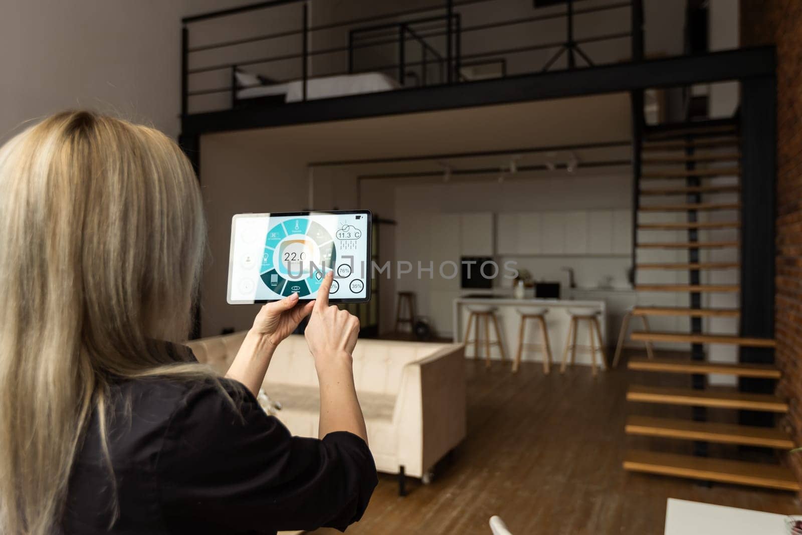 Woman controlling smart home devices using a digital tablet with launched application in the white room. Smart home concept.