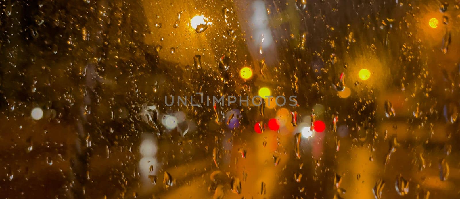 Rain bokeh road lights. Abstract shot of evening city traffic bokeh. Multicolored lights of the evening city and passing cars through a wet rainy window