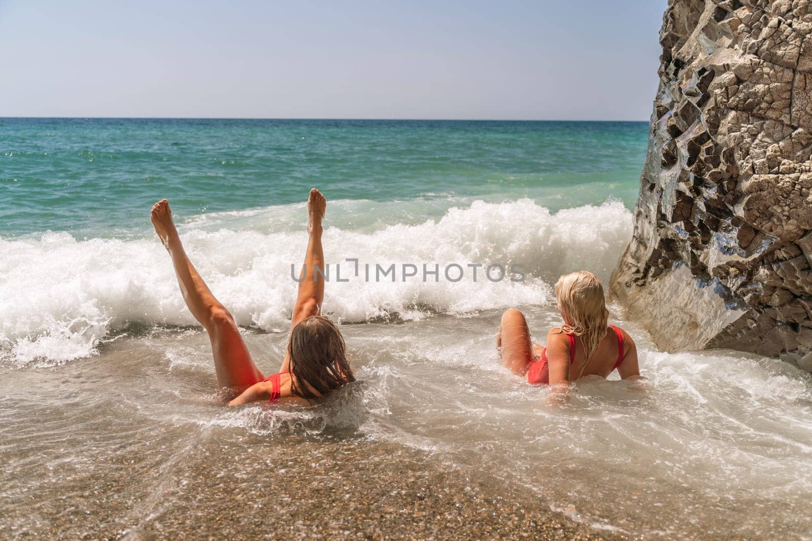 Women ocean play. Seaside, beach daytime, enjoying beach fun. Two women in red swimsuits enjoying themselves in the ocean waves