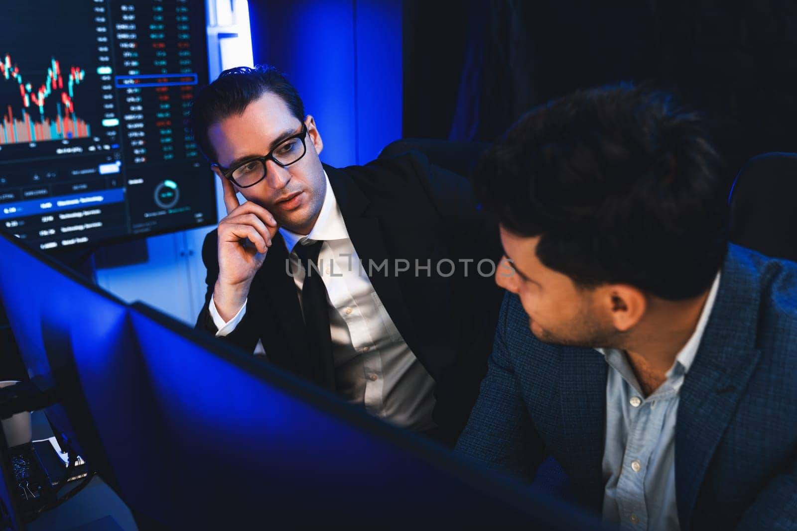 Two stock exchange traders discussing digital currency or market online focusing on dynamic data monitor. Concept of analyzing market stock cooperate at neon blue-light decorative workplace. Sellable.