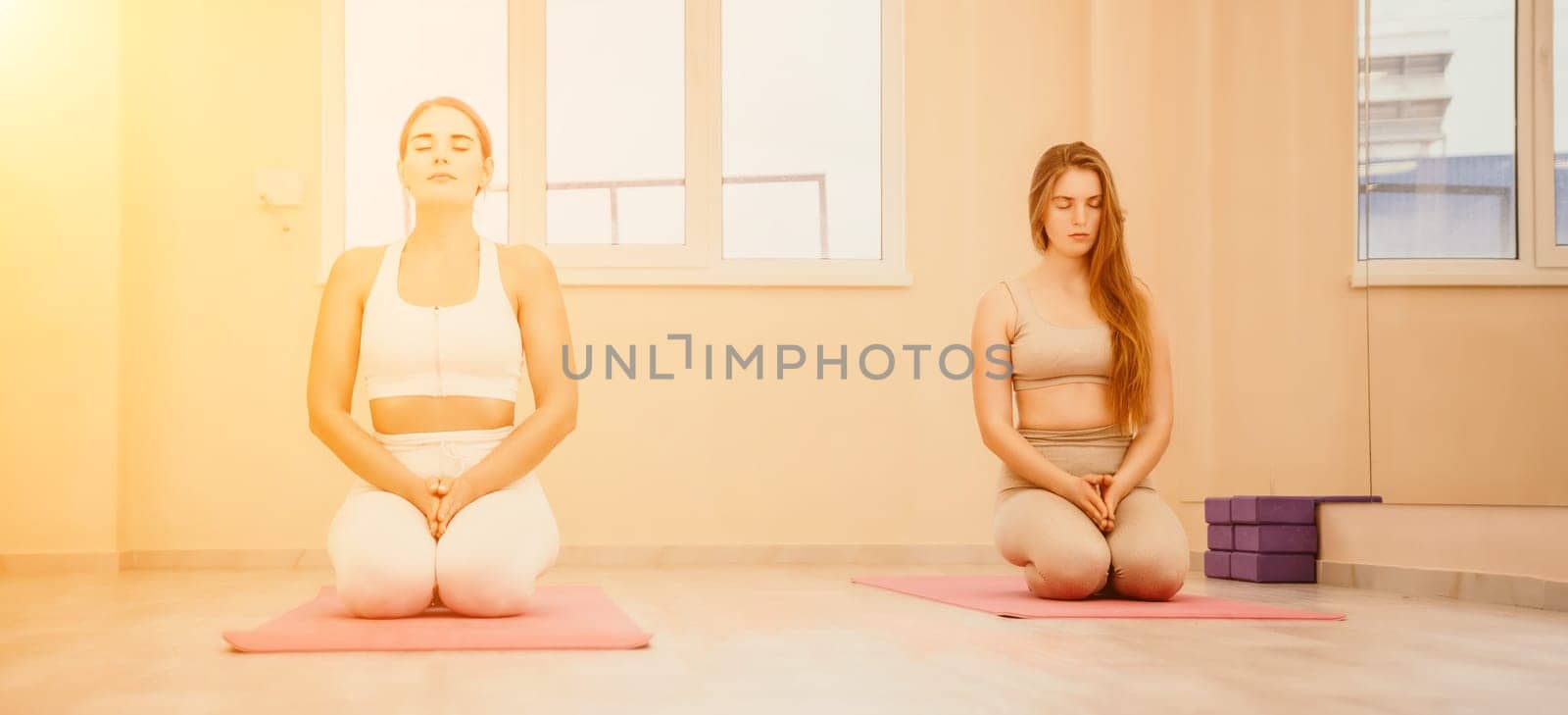 Group of young womans fitness instructor in Sportswear Leggings and Tops, stretching in the gym before pilates, on a yoga mat near the large window on a sunny day, female fitness yoga routine concept.