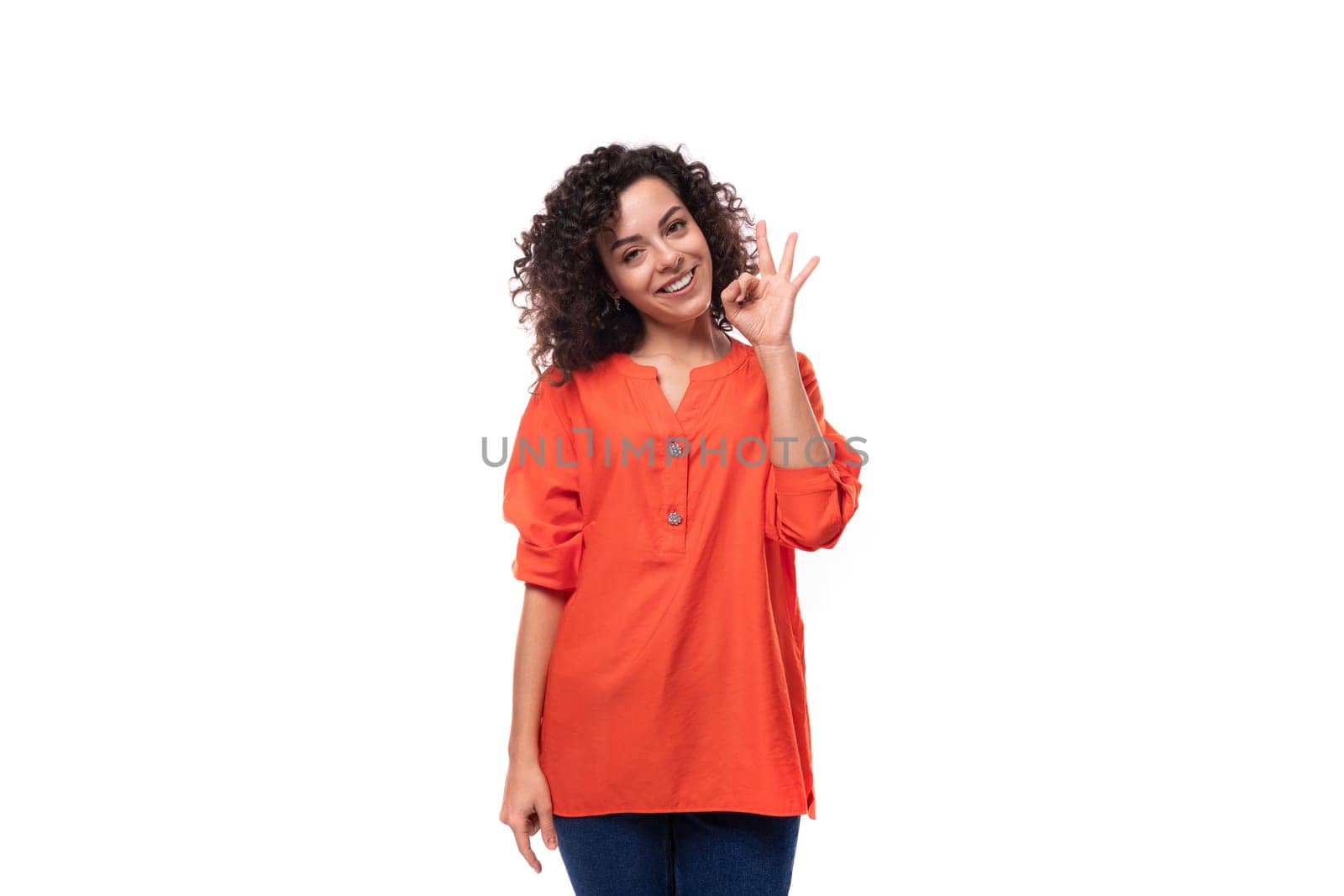 young european woman with curly black hair keeps dressed in a bright orange blouse works as an advertiser in the studio.