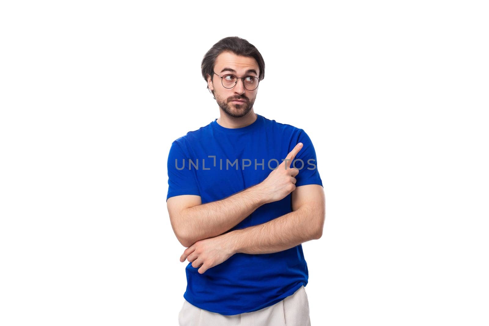 young confident brunette man with a beard dressed in a blue t-shirt shows his hand to the space for advertising on a studio white background.