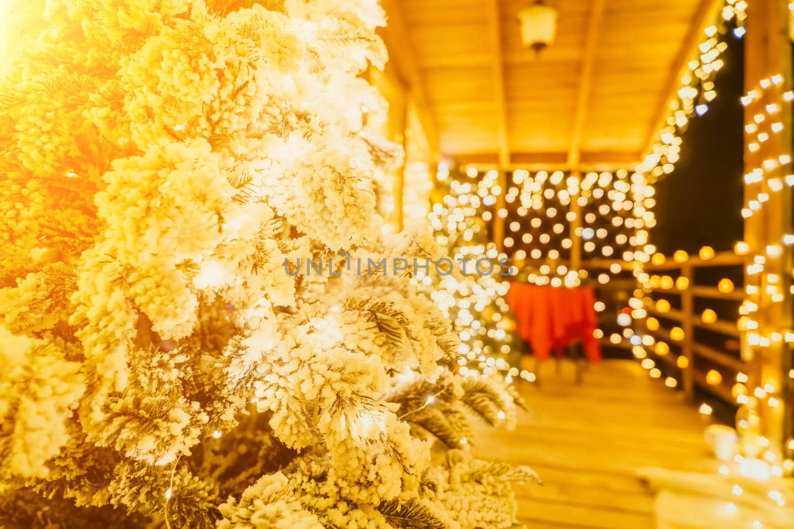Snow-covered Christmas tree with bright white lights situated outdoors near a building, a welcoming festive moment. by panophotograph