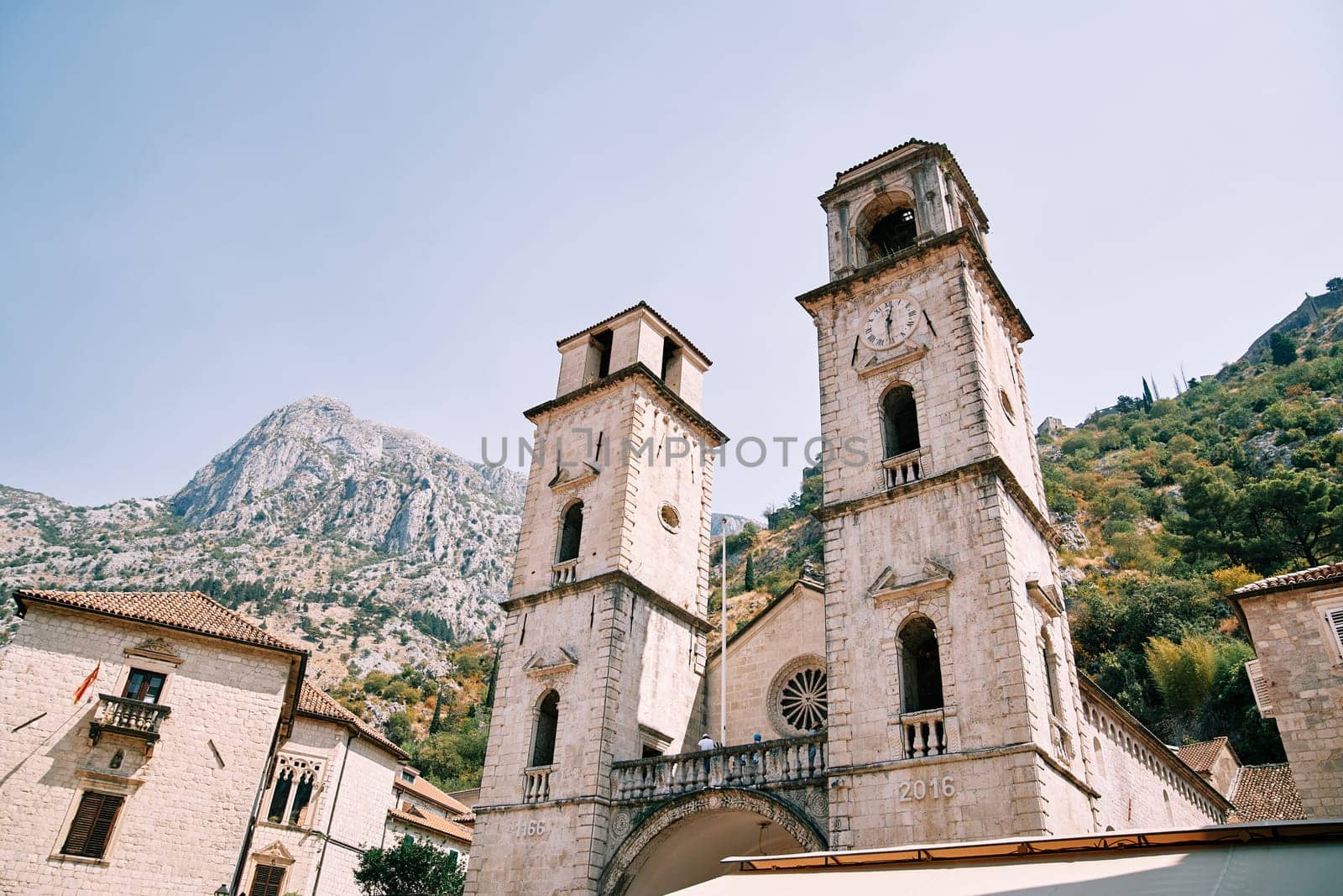 Bell towers of the Cathedral of St. Tryphon among ancient houses at the foot of the mountains. Kotor, Montenegro. High quality photo