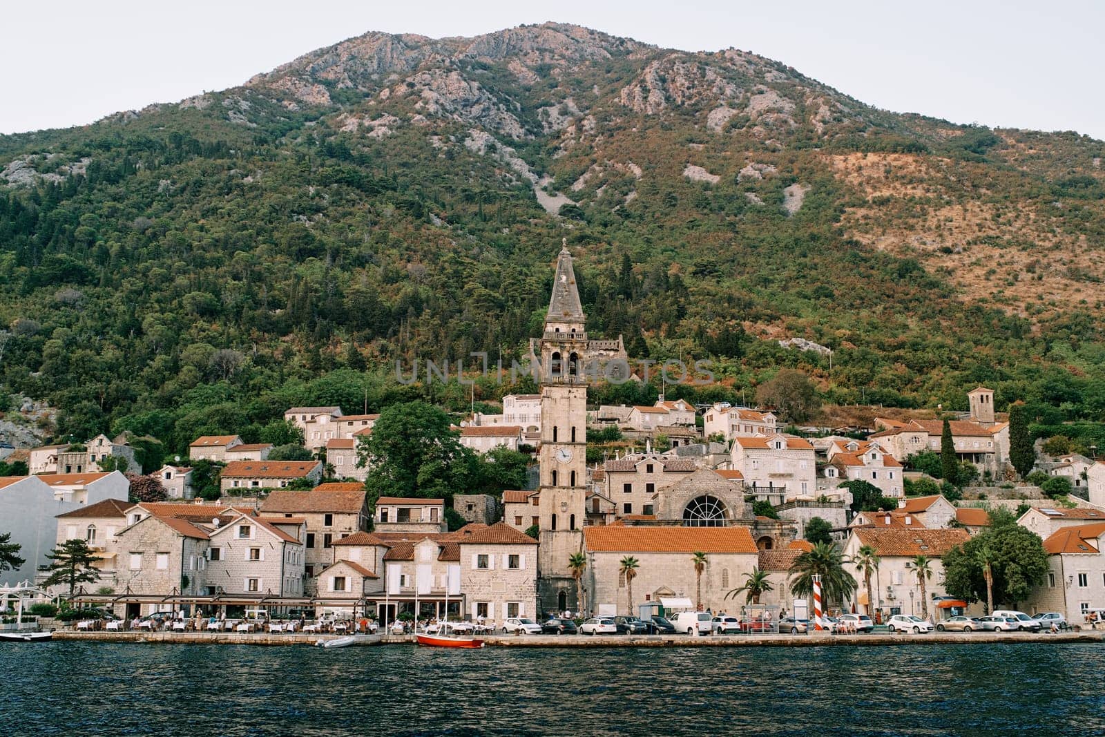 View from the sea of the bell tower of the Church of St. Nicholas among ancient houses at the foot of the mountains. Perast, Montenegro. High quality photo