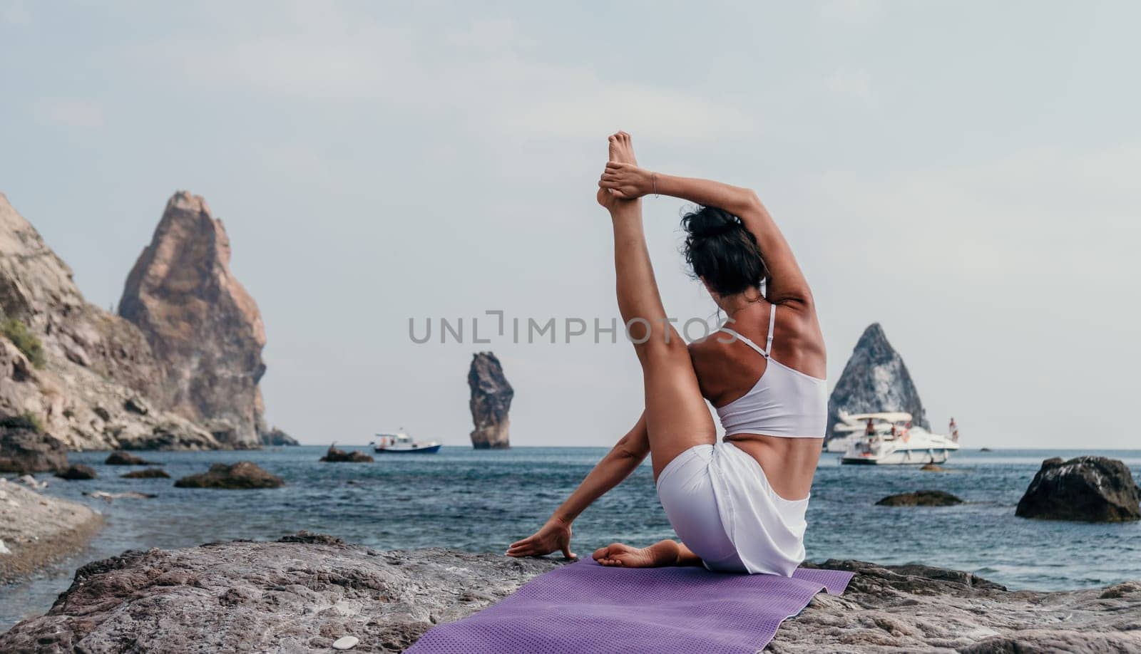 Fitness woman sea. A happy middle aged woman in white sportswear exercises morning outdoors on a beach with volcanic rocks by the sea. Female fitness pilates yoga routine concept. Healthy lifestyle. by panophotograph