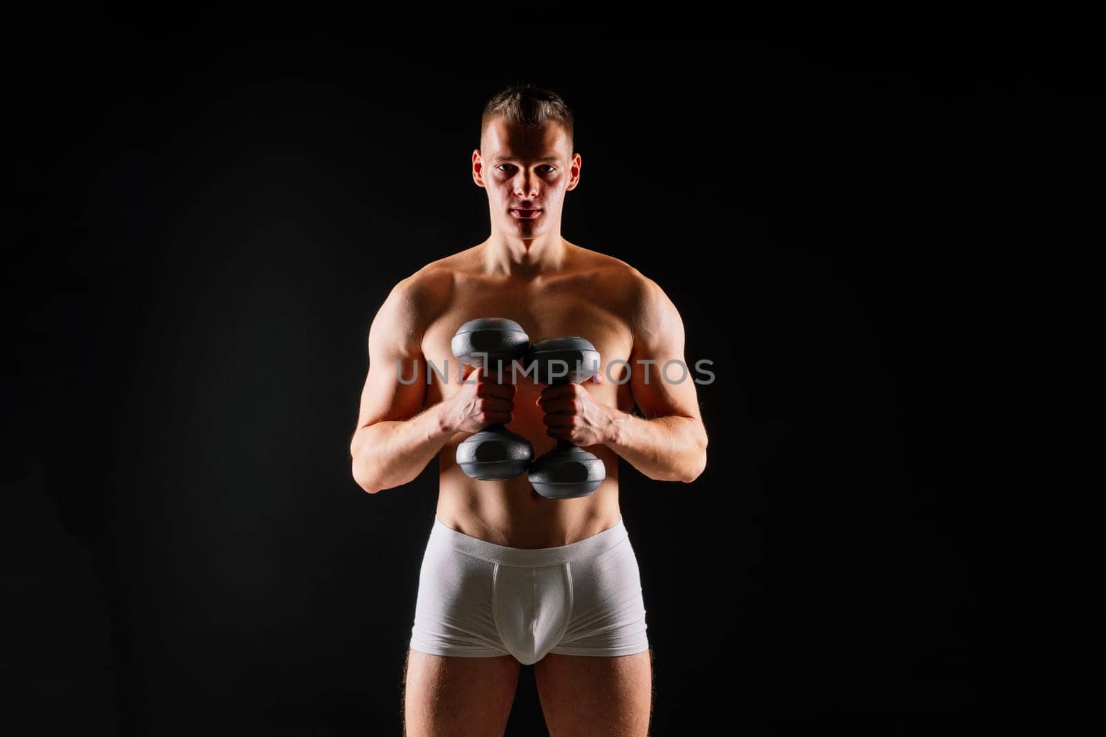 Man with pumped-up body with dumbbells in his hands white panties exercise