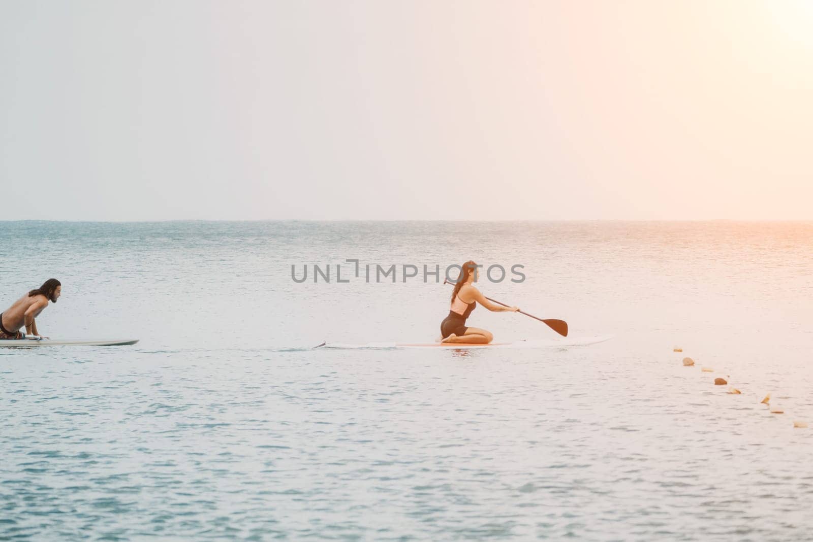 Sea woman and man on sup. Silhouette of happy young woman and man, surfing on SUP board, confident paddling through water surface. Idyllic sunset. Active lifestyle at sea or river