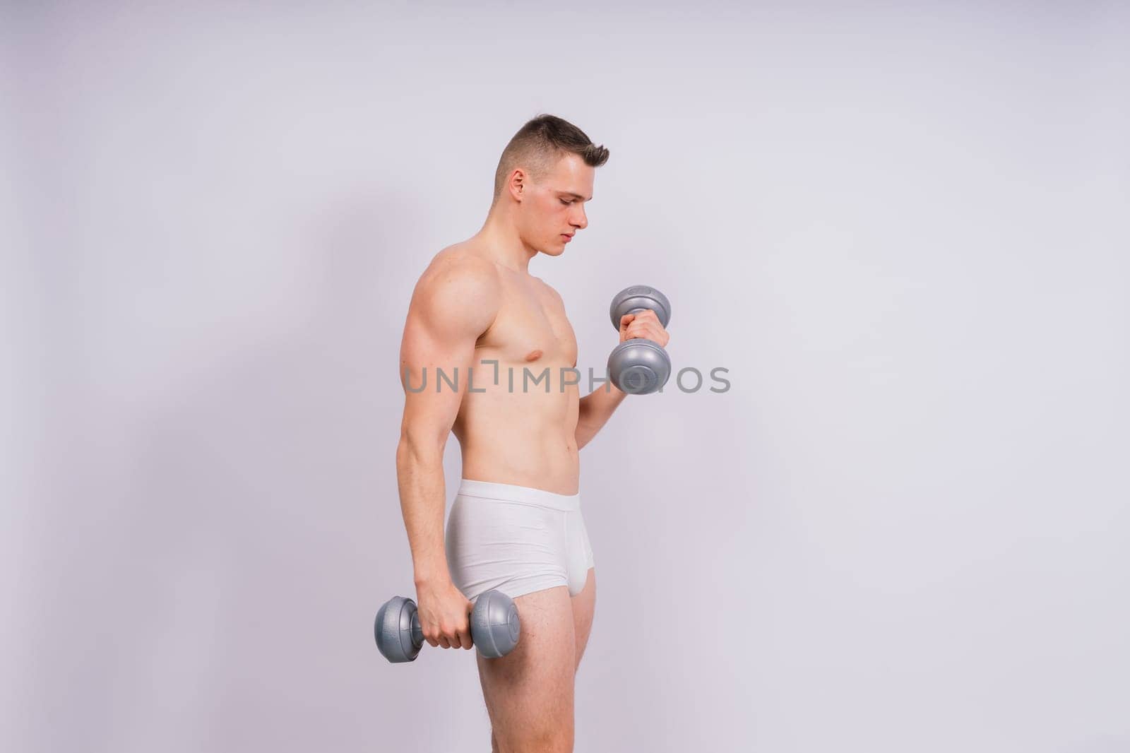 Man with pumped-up body with dumbbells in his hands white panties exercise