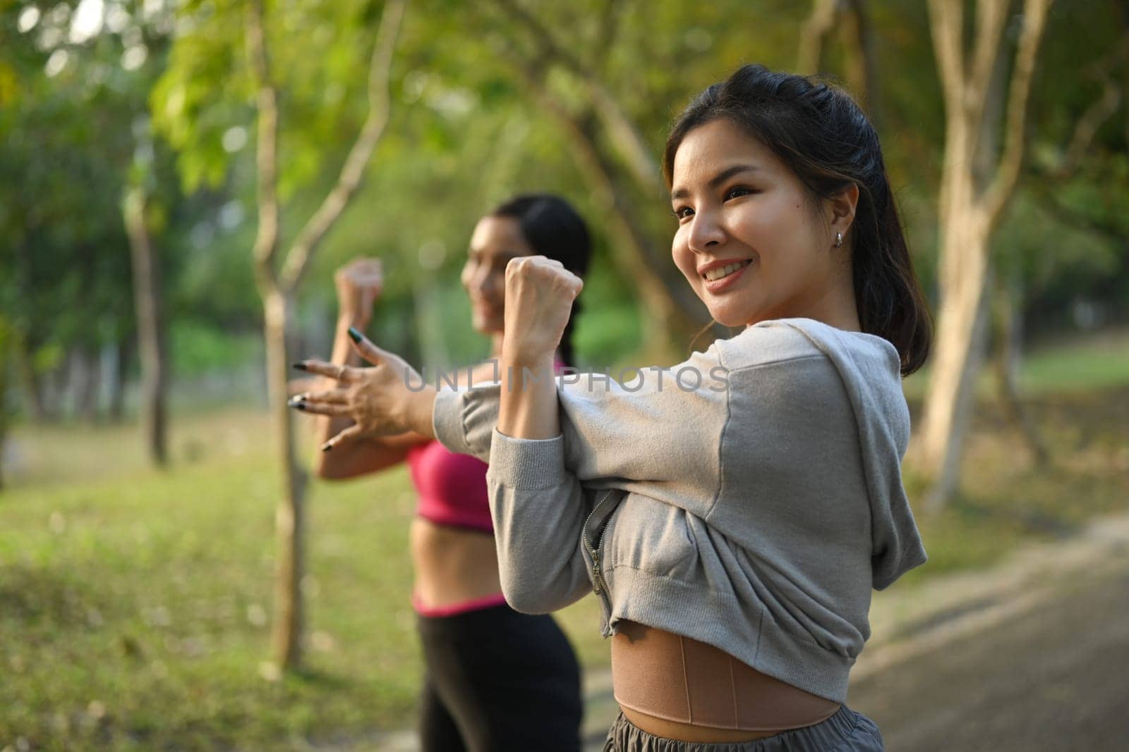 Two beautiful young sporty women doing stretching exercises before running in the summer park.