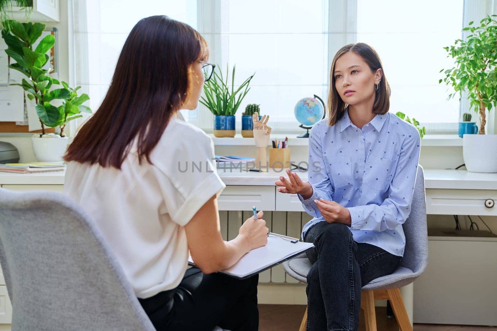 Young woman at a mental therapy session talking to female psychologist in therapist's office. Serious female patient, help support professional counselor, psychotherapist, mental health youth concept