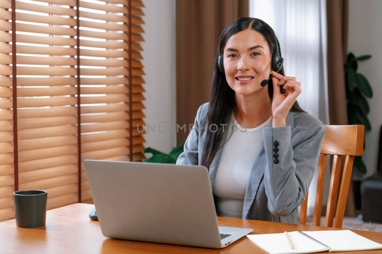 Female call center operator or customer service helpdesk staff working on workspace while talking on the headset to provide assistance for customer. Professional modern business service. Blithe