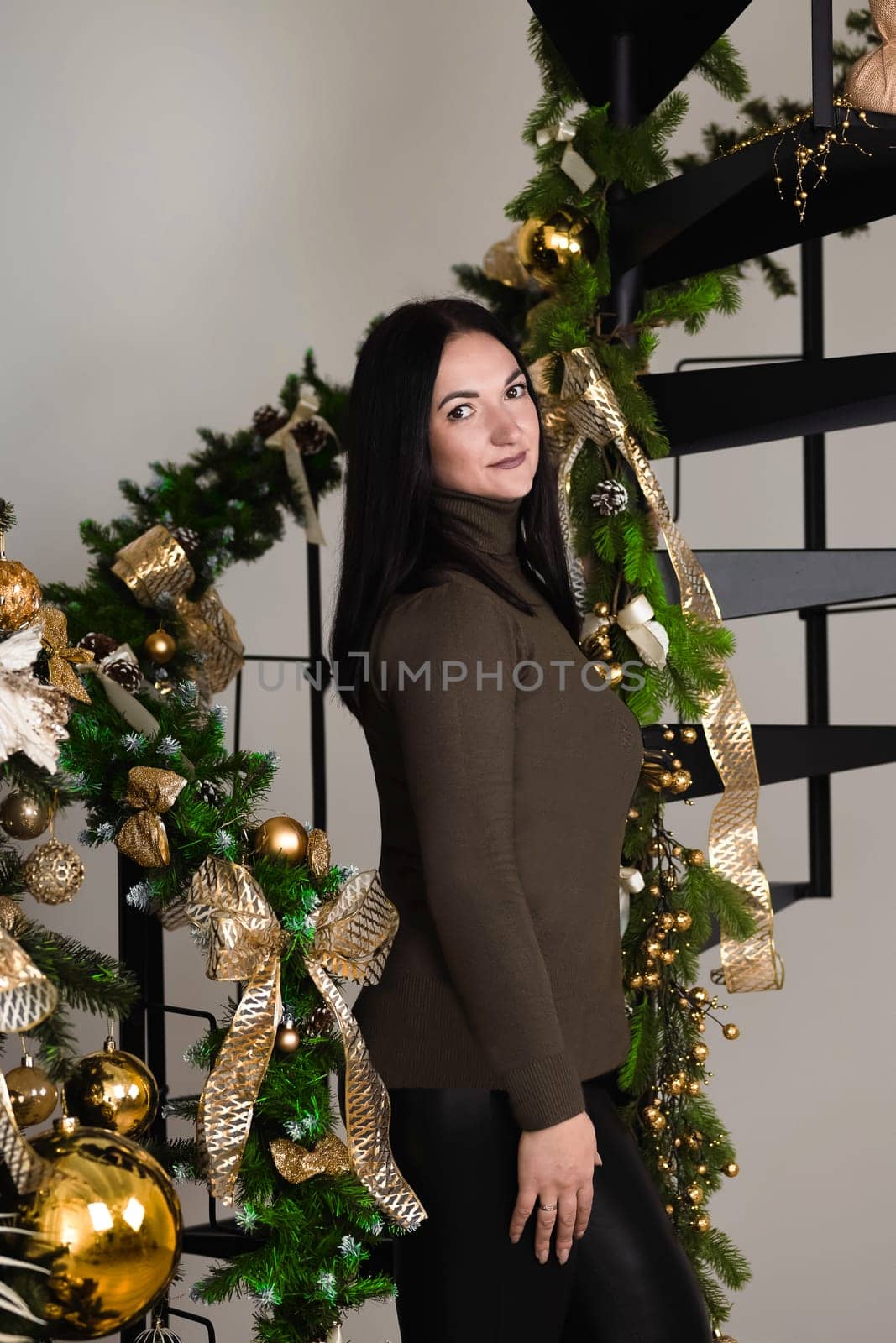 A brunette girl stands next to Christmas decorations near the stairs in the studio