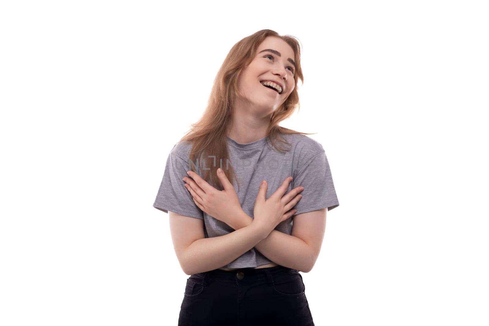 Teenage girl with blond hair in a gray T-shirt laughs on a white background by TRMK