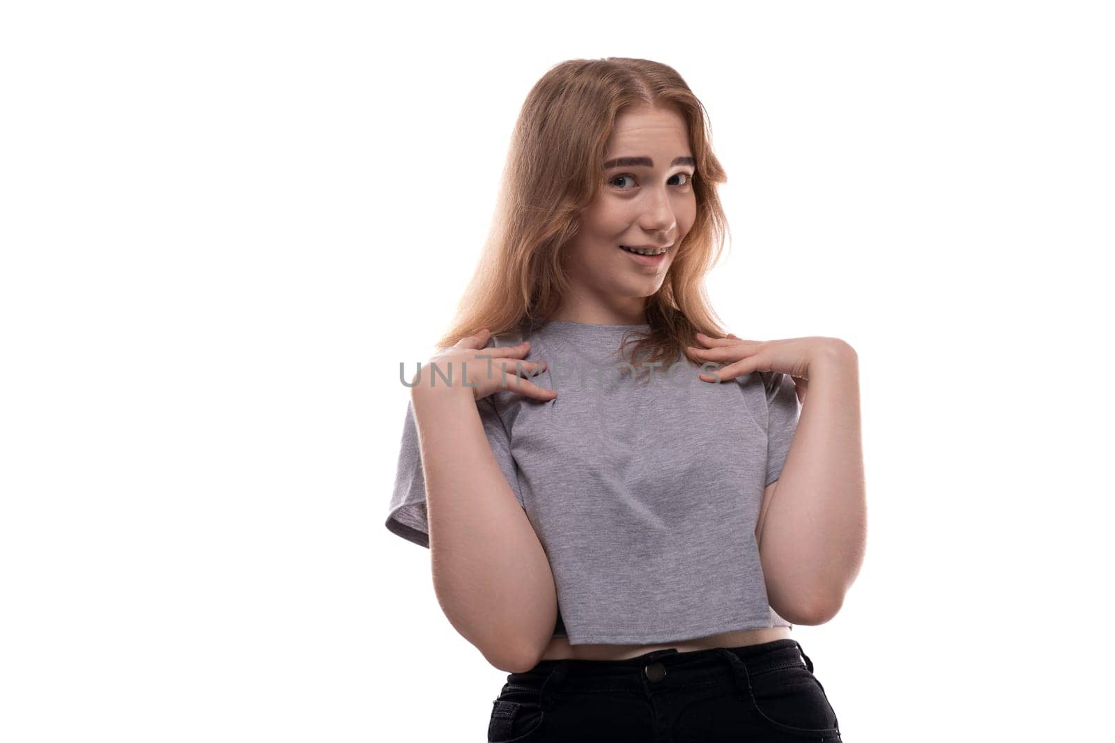 Confused fair-haired teenage girl in a gray T-shirt on a white background.