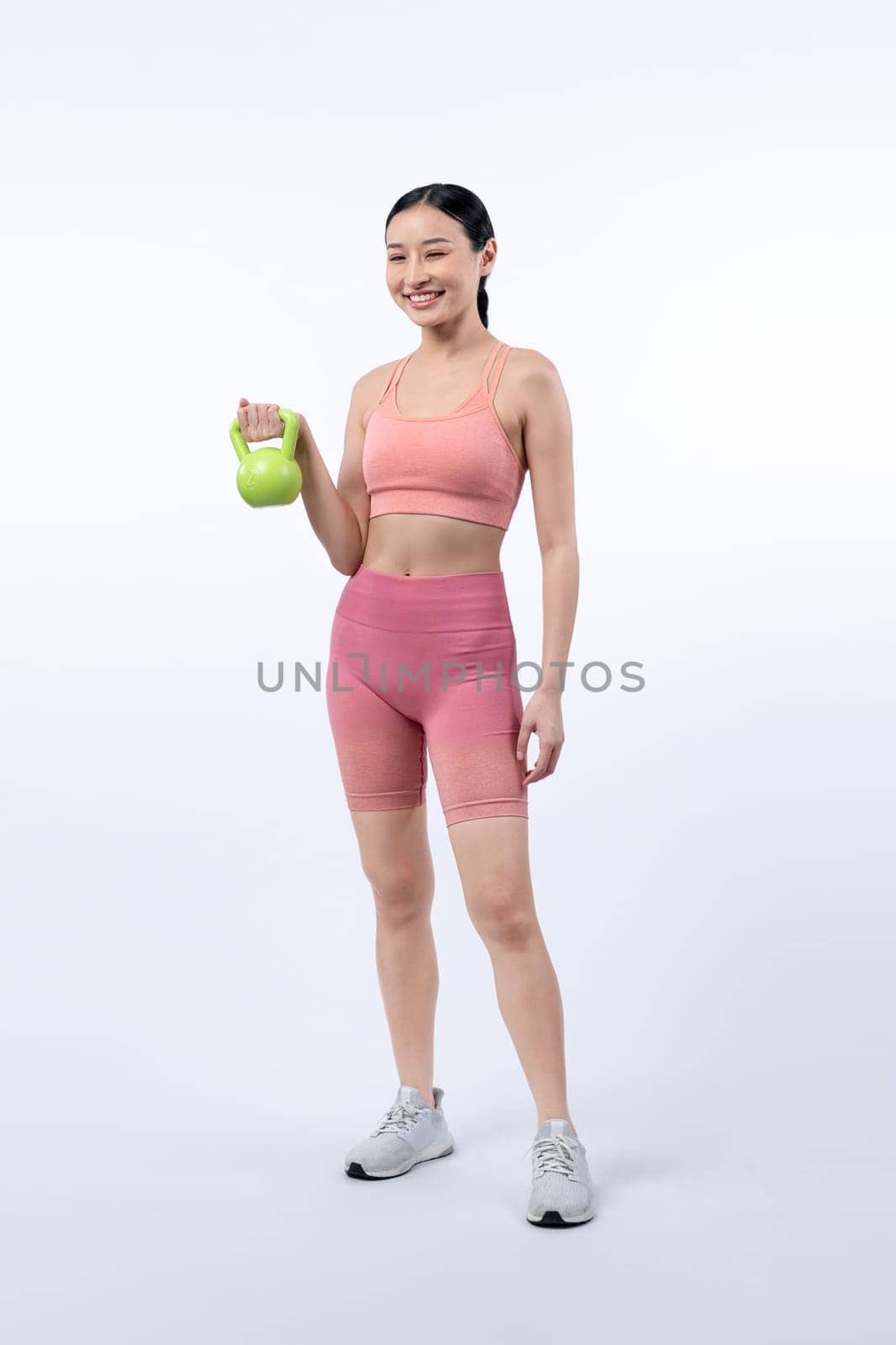 Vigorous energetic woman doing kettlebell weight lifting exercise on isolated background. Young athletic asian woman strength and endurance training session as body workout routine.