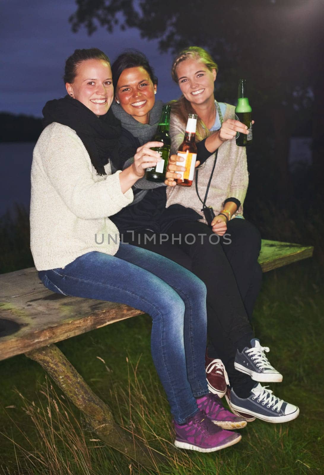 Friends, portrait and beer outdoor at night for camping adventure, nature celebration or group connection. Woman, face and smile for alcohol drinking or cheers toast for summer, travel or vacation by YuriArcurs