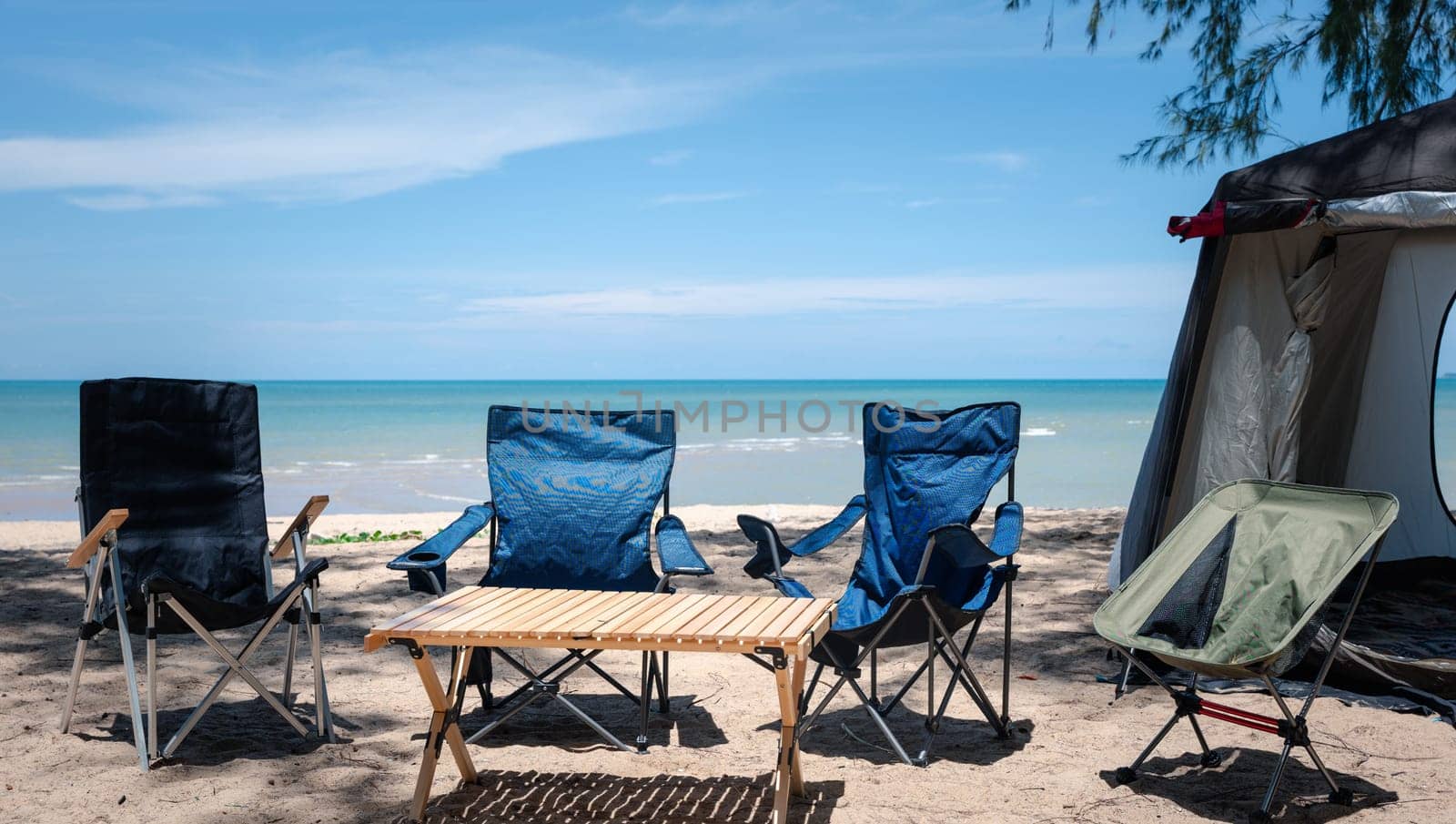 Beachfront campsite, Empty chairs, picnic table, and a tent under the summer sun. Find happiness in outdoor adventures, family time, and the beauty of nature. The sea is where it all begins.
