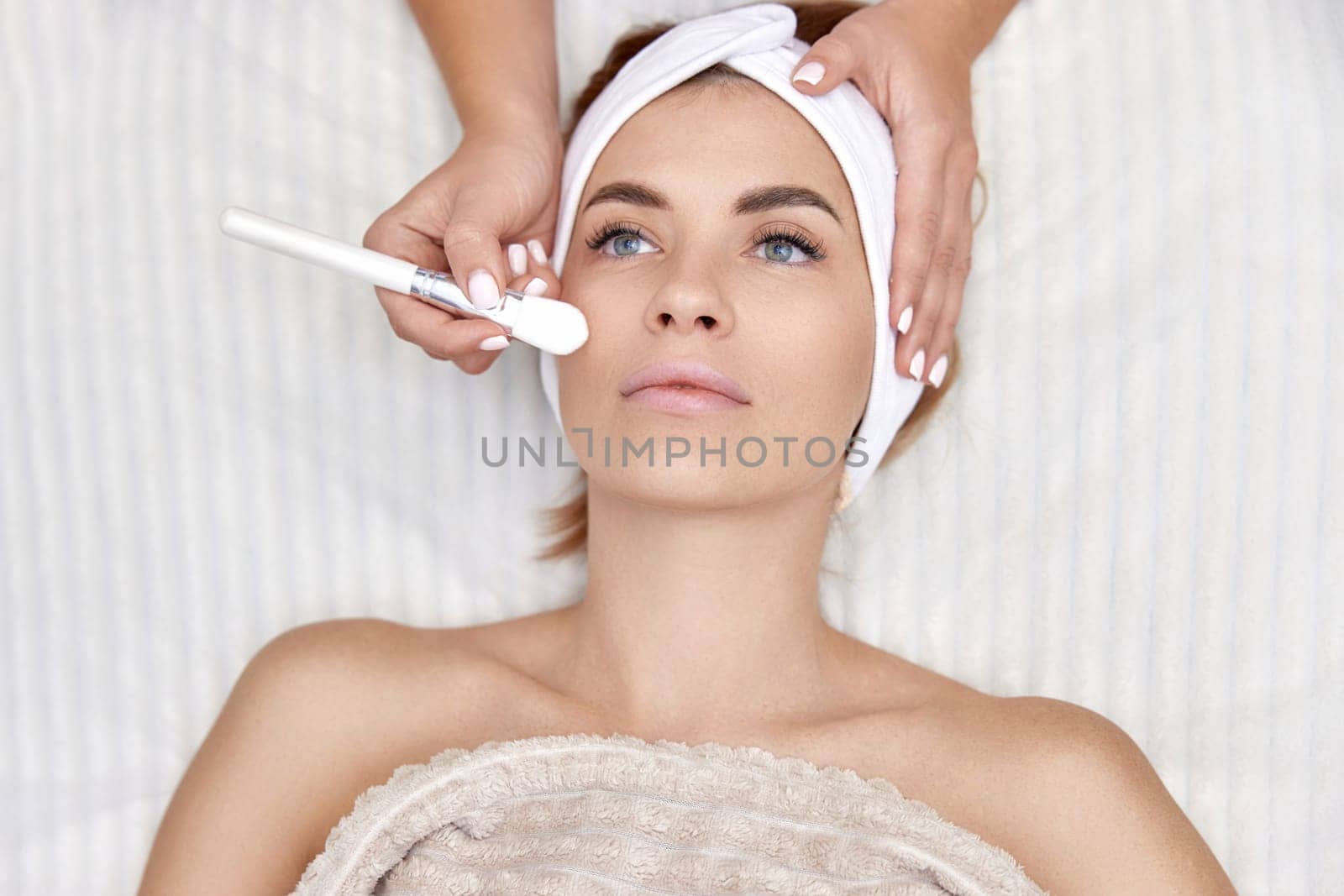 female hand touching the patient's face with a brush. beautician applies the mask to female face. facial skin care. top view
