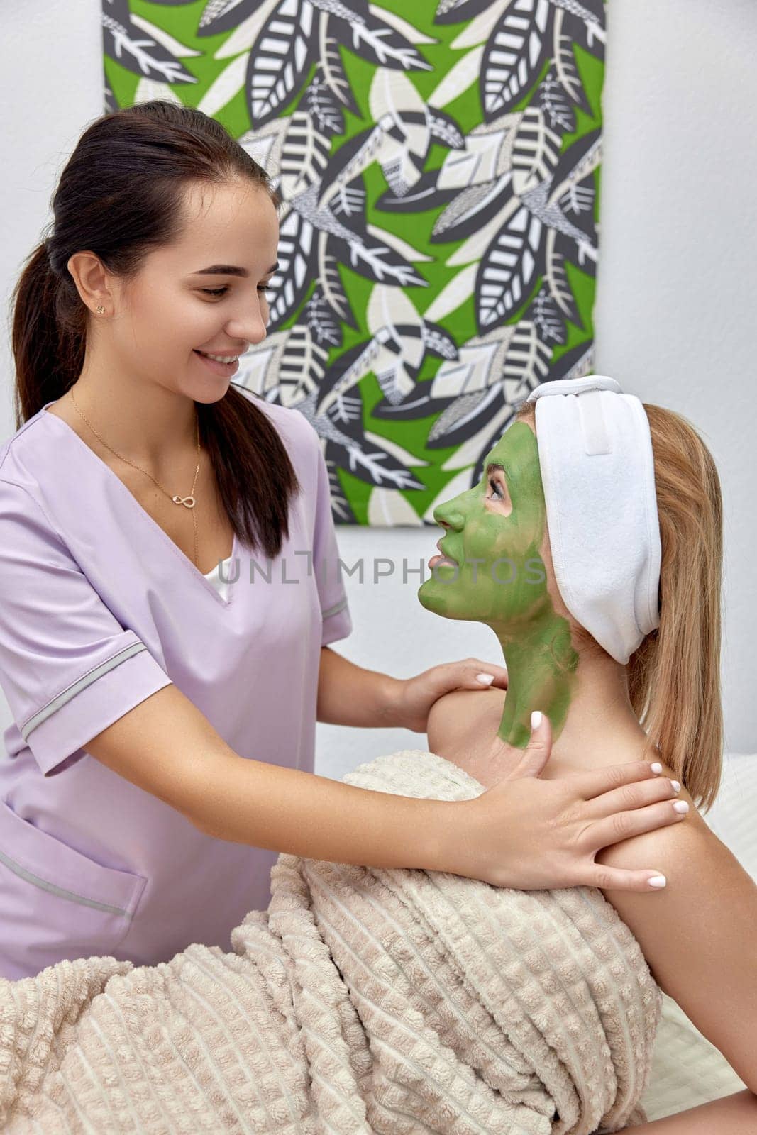 happy female cosmetologist talking with woman client in beauty clinic.